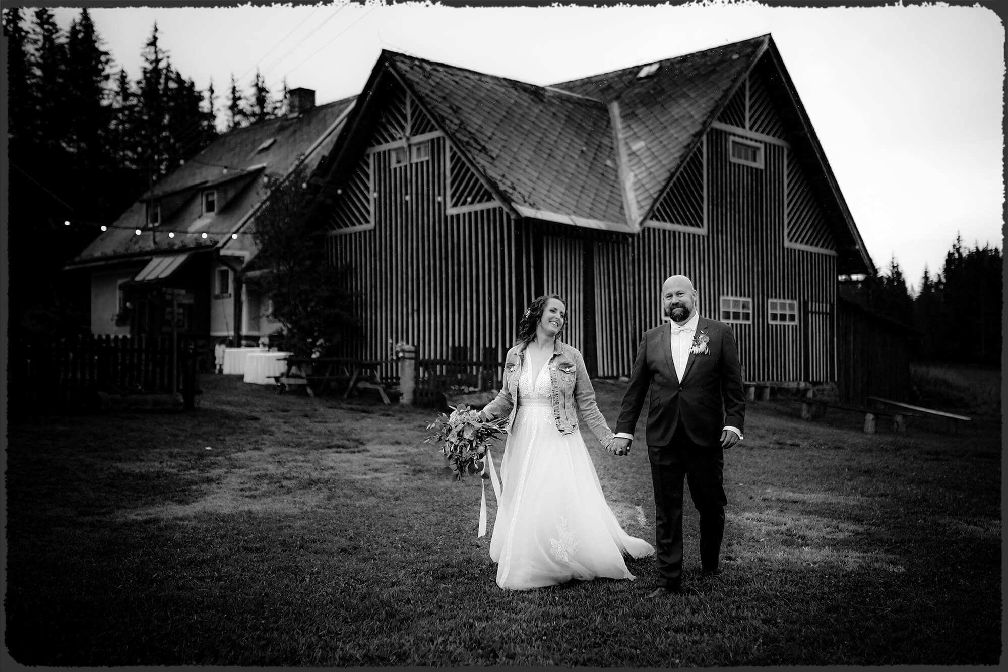 Svatební fotografie novomanželů se stodolou za zády.