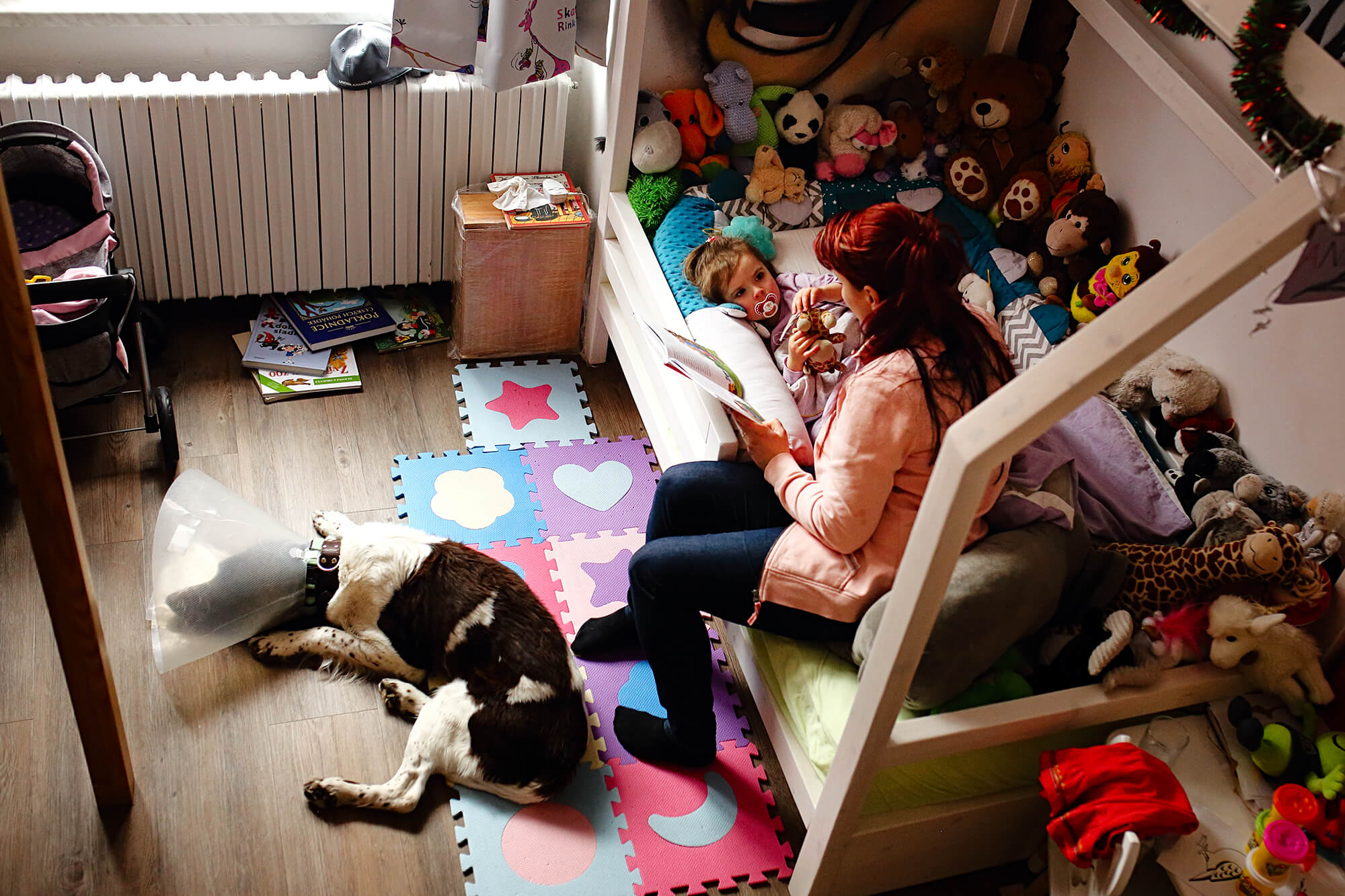Dokumentární fotografie maminky, která čte dceři knížku před spaním.