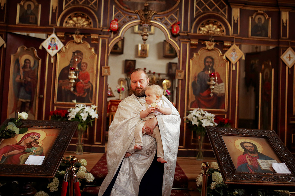 dokumentární fotografie z křtin. Chrám svatých Cyrila a Metoděje a v něm biskup křtí chlapečka.
